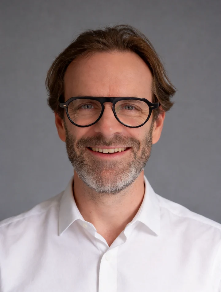 Portrait de Thibaut, souriant, avec des lunettes et une chemise blanche